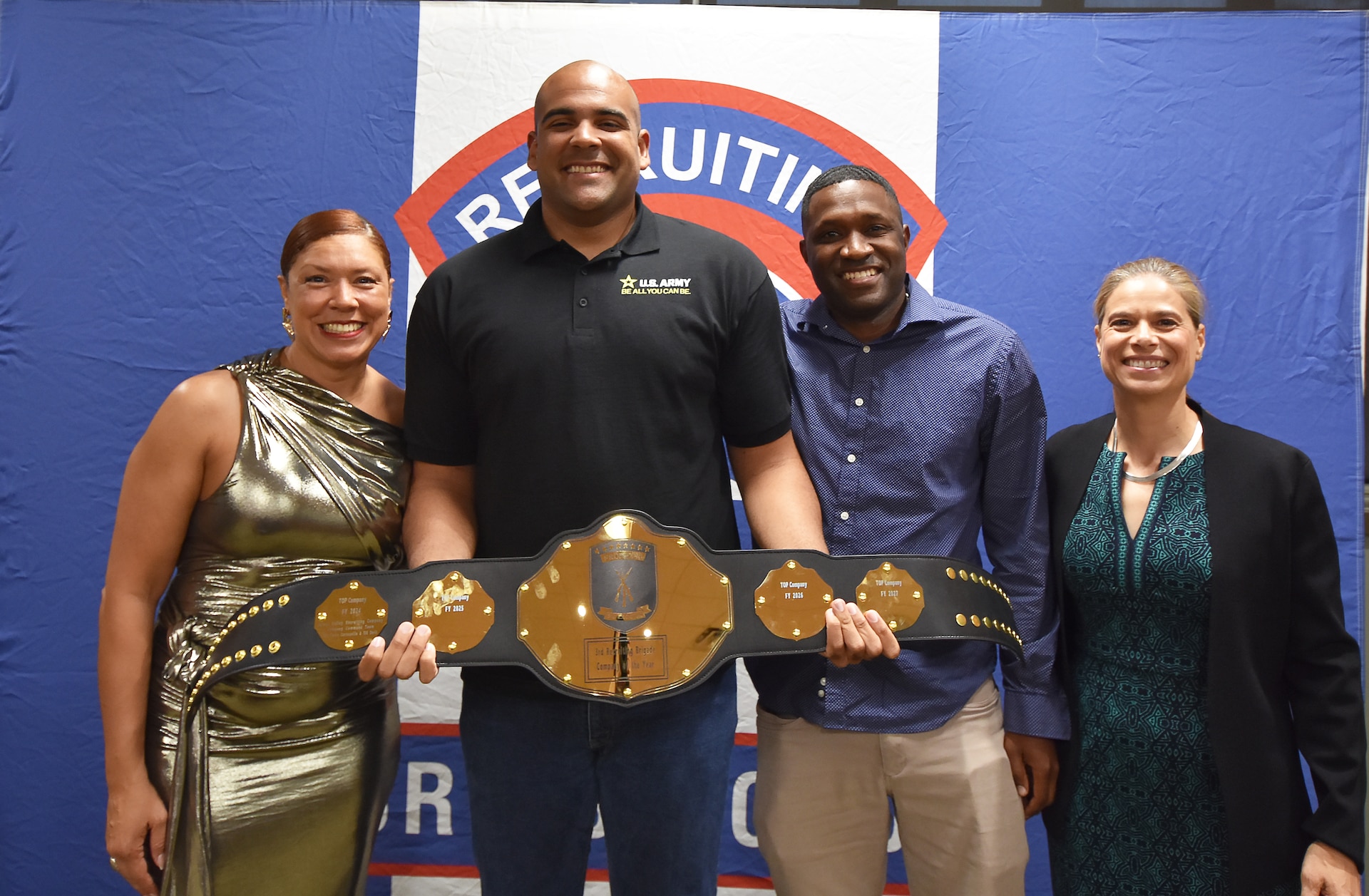 Two male Army Soldiers smile while holding a gold belt.  On either side are smiling female Soldier award presenters.