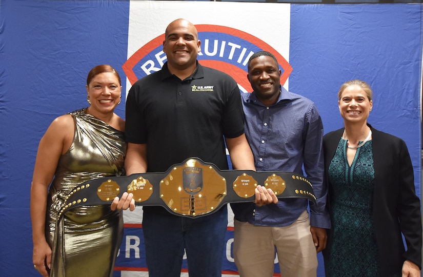 Two male Army Soldiers smile while holding a gold belt.  On either side are smiling female Soldier award presenters.