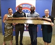 Group of four Soldiers in civilian dress hold up an award plaque in front of Army Recruiting Third Brigade backdrop.