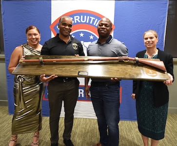 Group of four Soldiers in civilian dress hold up an award plaque in front of Army Recruiting Third Brigade backdrop.