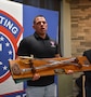 Man poses with trophy plaque featuring two sabers representing the Army Noncomissioned Officer