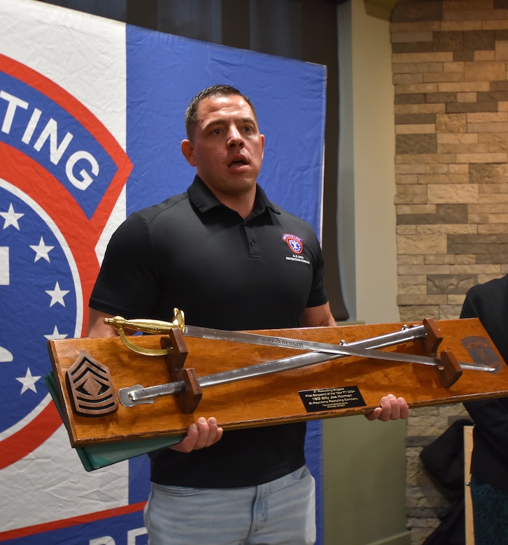 Man poses with trophy plaque featuring two sabers representing the Army Noncomissioned Officer