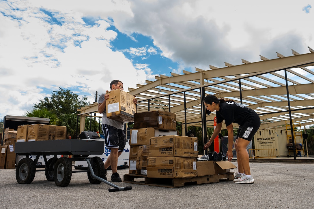 Marines in athletic clothing sort through boxes on a pallet during daylight.