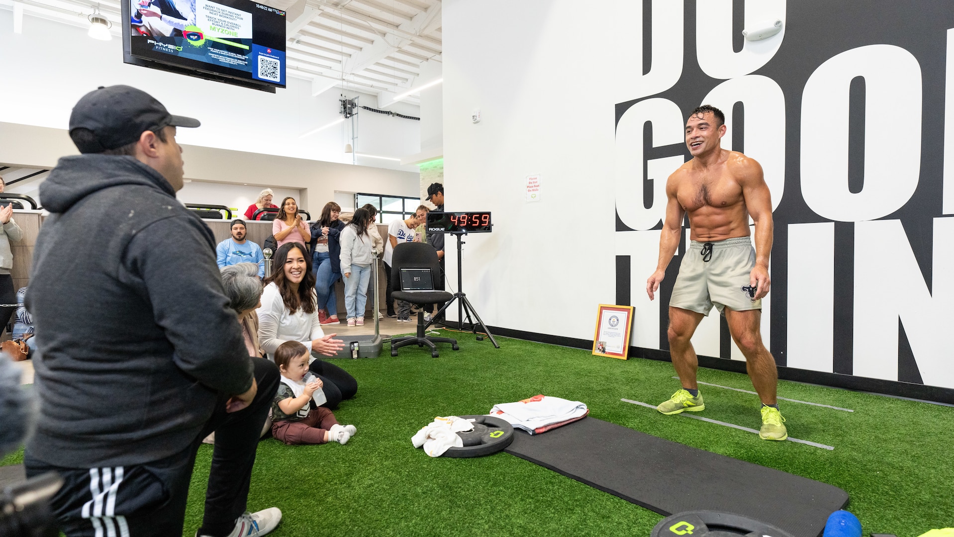 A moment of triumph during Maj. Tommy Vu's world record attempt at a gym in Salem, Ore., Oct. 5, 2024. From left: Pedro Velasquez, Oregon National Guard state equal employment manager; Linda Vu, the major's wife holding son Adonis; and Maj. Tommy Vu as he nears his goal of 1,027 chest-to-ground burpees in one hour.