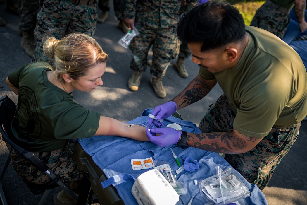 240908-M-AO923-1102 U.S. Navy Hospital Corpsman 2nd Class Antonio Coss inserts an IV catheter needle into the arm of U.S. Marine Corps Cpl. Donna Windwehen during Artillery Relocation Training Program 24.2 at the Yausubetsu Maneuver Area, Hokkaido, Japan, Sept. 9, 2024. ARTP, established by the 1997 Special Action Committee in Okinawa, relocates live-fire artillery training from Okinawa to mainland Japan to maintain readiness and stabilize U.S. Forces’ basing, enhancing regional security across Japan and the Indo-Pacific. This Training boosts the capabilities and readiness of the Marine Corps’ only permanently forward-deployed artillery unit, enabling accurate indirect fire support. Coss, a native of Texas, is a corpsman with 3d Battalion, 12th Marine Littoral Regiment, 3d Marine Division. Windwehen, a native of Louisiana, is an ammunition technician with 12th Marine Littoral Regiment, 3d Marine Division. (U.S. Marine Corps photo by Lance Cpl. Matthew Morales)