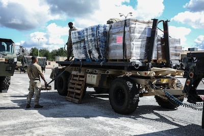 Soldiers stand around or on top of a truck with pallets of supplies
