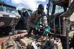 A black soldier in camo stands over gas cans with a fuel hose.
