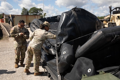 A male and female soldier stand around a black inflatable float.