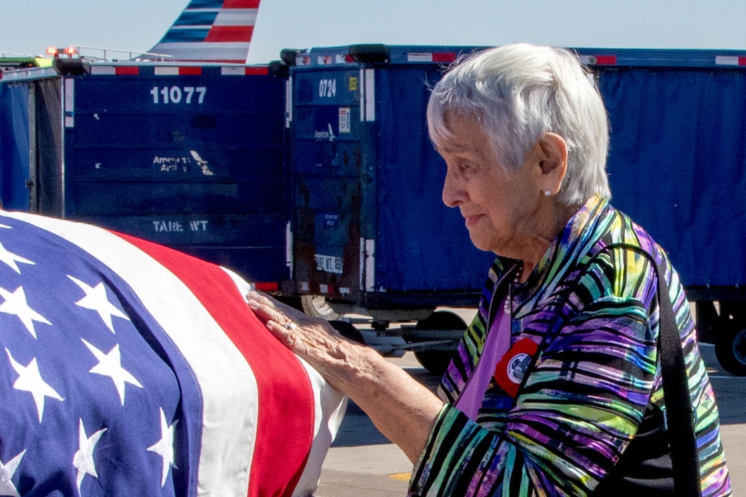 A person using a cane rest their hand on a casket covered with an American flag.