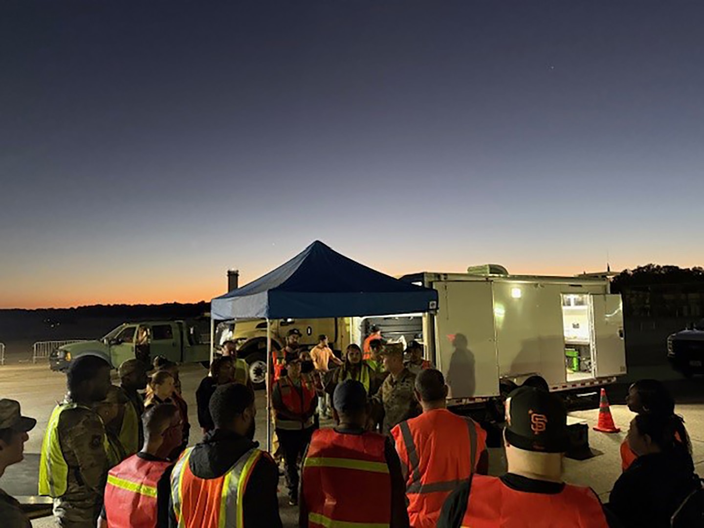 A group of people in reflective vests stand outside at dusk.