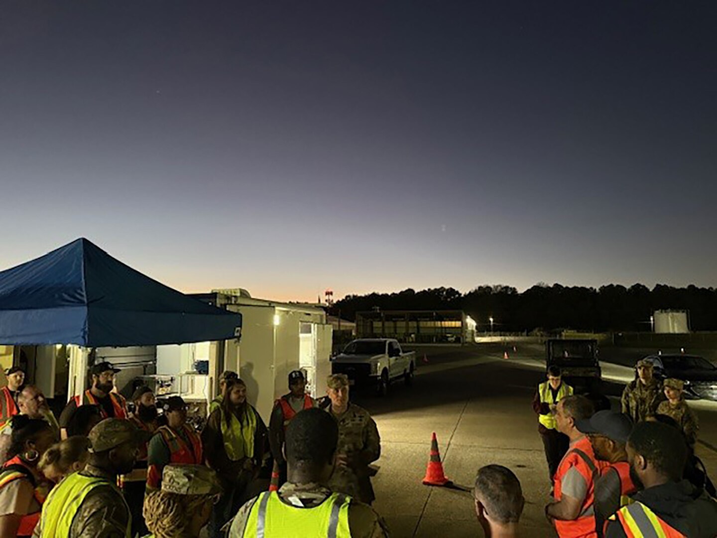 A group of people in reflective vests stand outside at dusk.