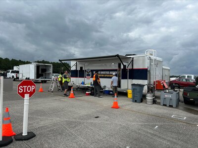Trailers are parked outside in a parking lot with people walking around in reflective vests.