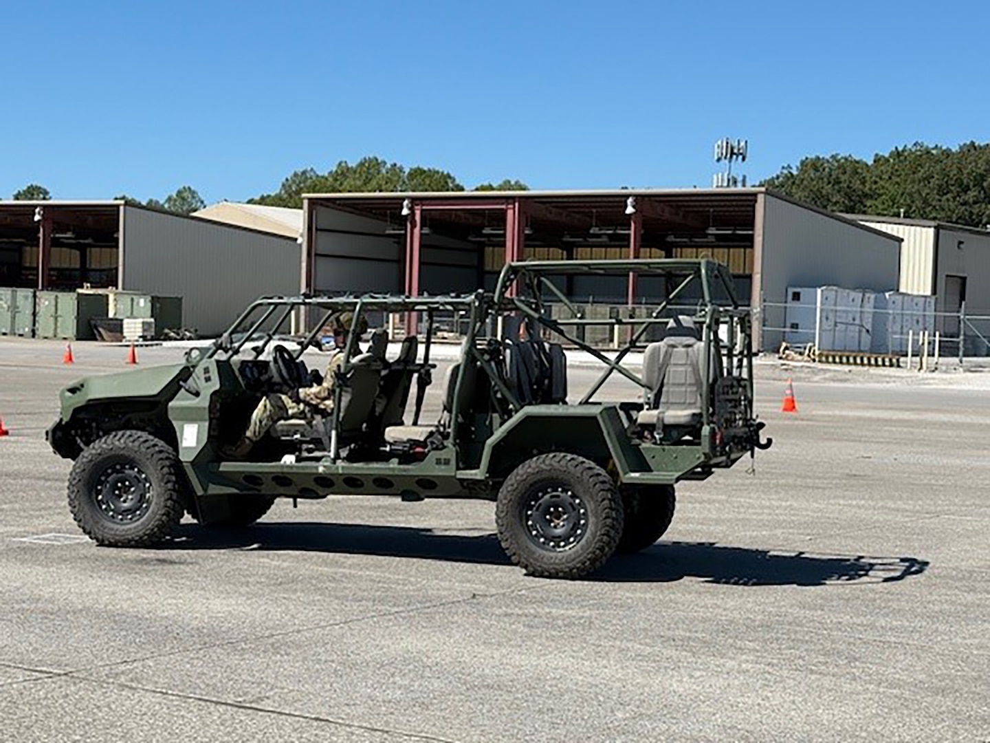 An Army soldier in camouflage drives a support vehicle across an empty lot.