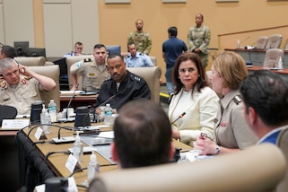 Military officials sit around a conference table and talk.