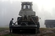 Staff Sgt. Parker Kessel (left) and Staff Sgt. Joseph Armstrong (right) from the 357th Engineer Company secure a military DR7 II CAT Dozer onto a transport trailer on October 5, 2024, before moving out it to clear debris from a nearby road where residents were trapped. The Army Reserve engineers were deployed early in the morning to restore road access for the local community in Burnsville, North Carolina (Yancey County).