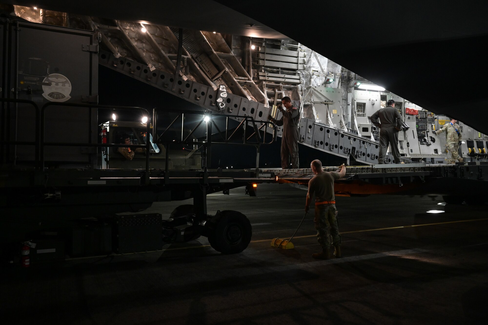 Airmen unload cargo from a C-17 Globemaster III aircraft onto a k-loader at night.