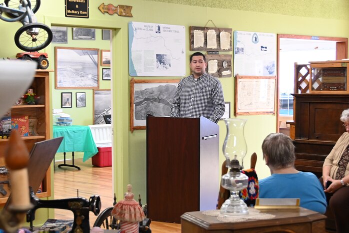 A man in a button-up shirt gives a speech to a small crowd from behind a podium at a local museum.