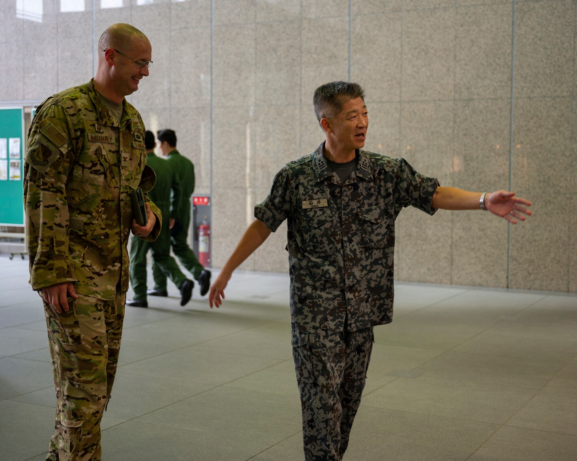 A Japanese military member leads a U.S. military member inside a building.