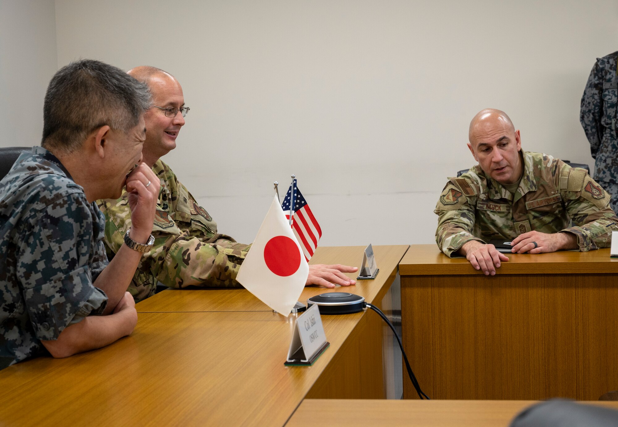Three military members sit a wooden tables.