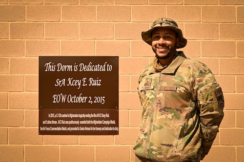 An Airman poses for a photo next to a plaque.