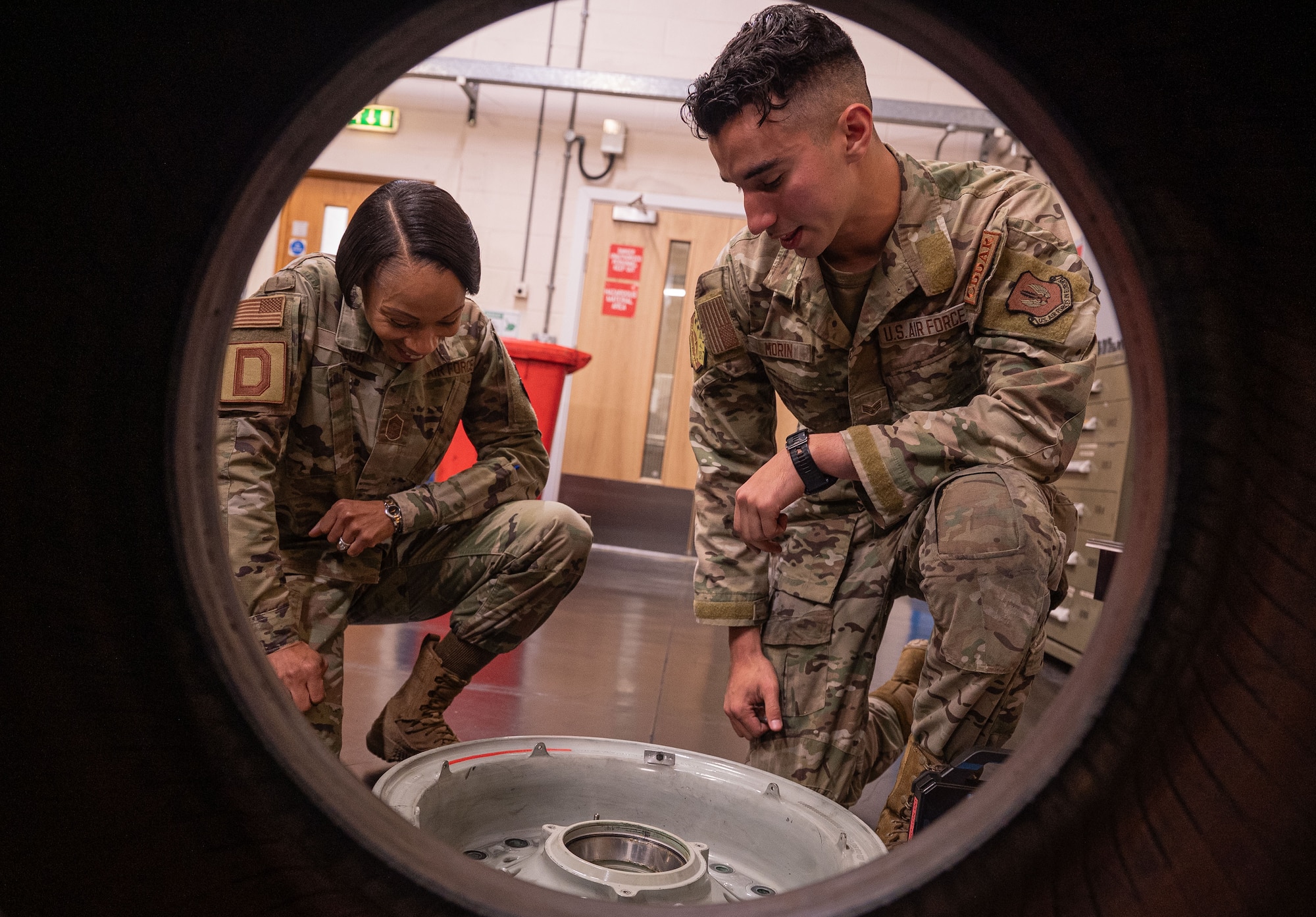 U.S. Air Force Chief MSgt. Tiffany Griego, left, 100th Air Refueling Wing command chief, and Senior Airman Nathaniel Morin, 100th Aircraft Maintenance Squadron repair and reclamation journeyman, look at an aircraft wheel rim at Royal Air Force Mildenhall, England, Oct. 4, 2024.