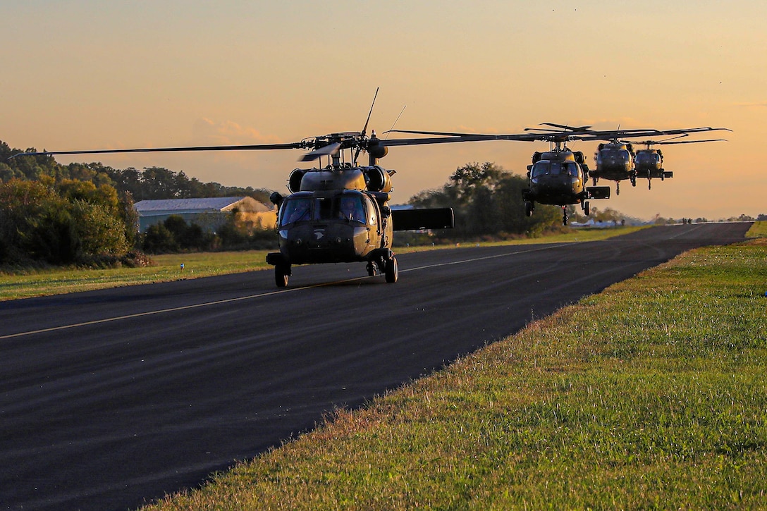 Four Army helicopters arrive to provide hurricane relief on a hazy day.