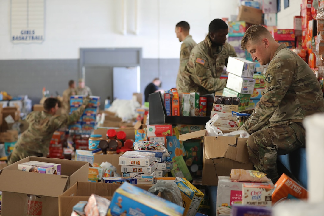 Soldiers sort food donations in boxes in a storage area.