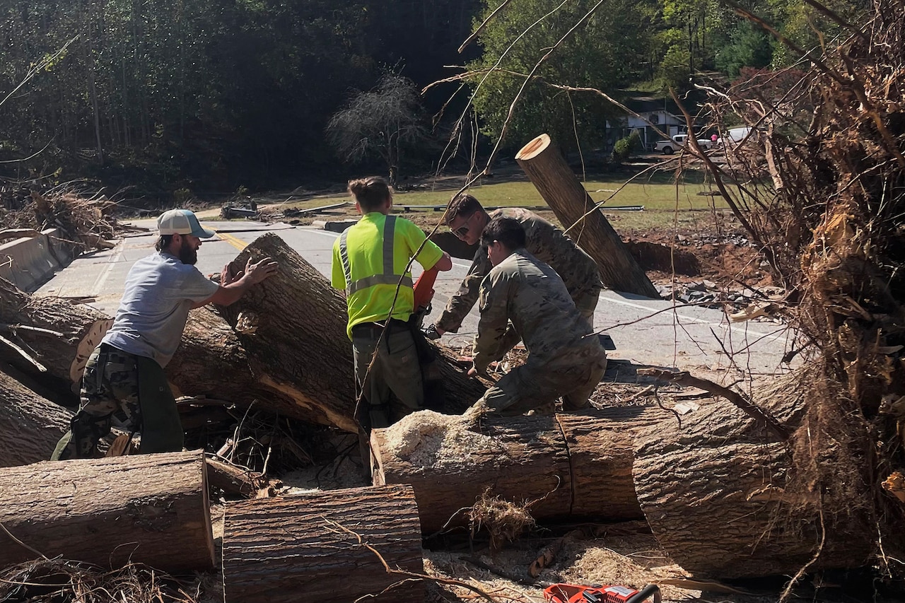 A group of people clear large tree trunks from a road.
