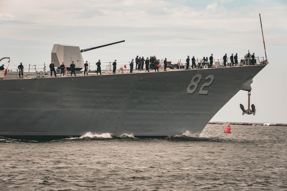 Sailors stand watch aboard a partially visible ship in body of water on a gloomy day.