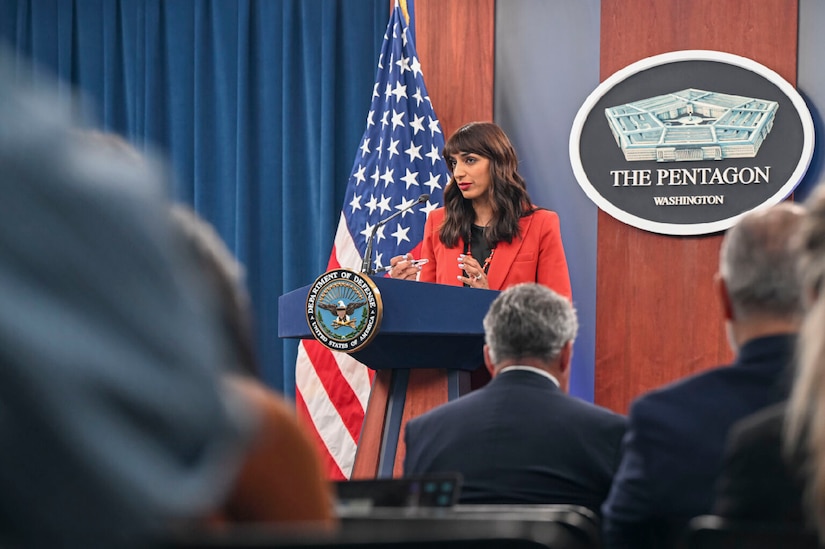 A woman stands behind a lectern. Behind her is a sign that says, "The Pentagon -- Washington."