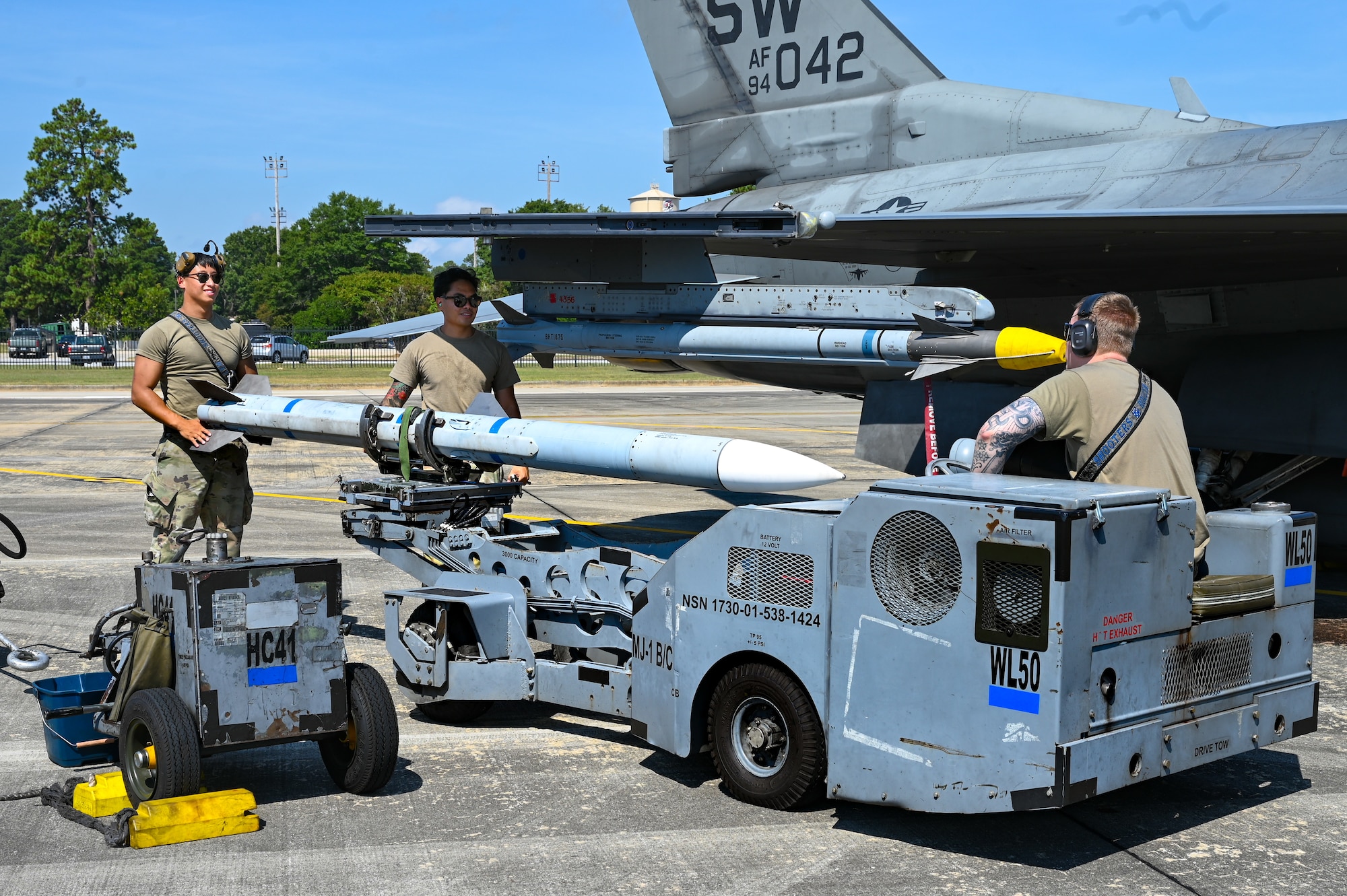 Three Airmen load an AIM-120 advanced medium-range air-to-air missile onto an F-16C Fighting Falcon.