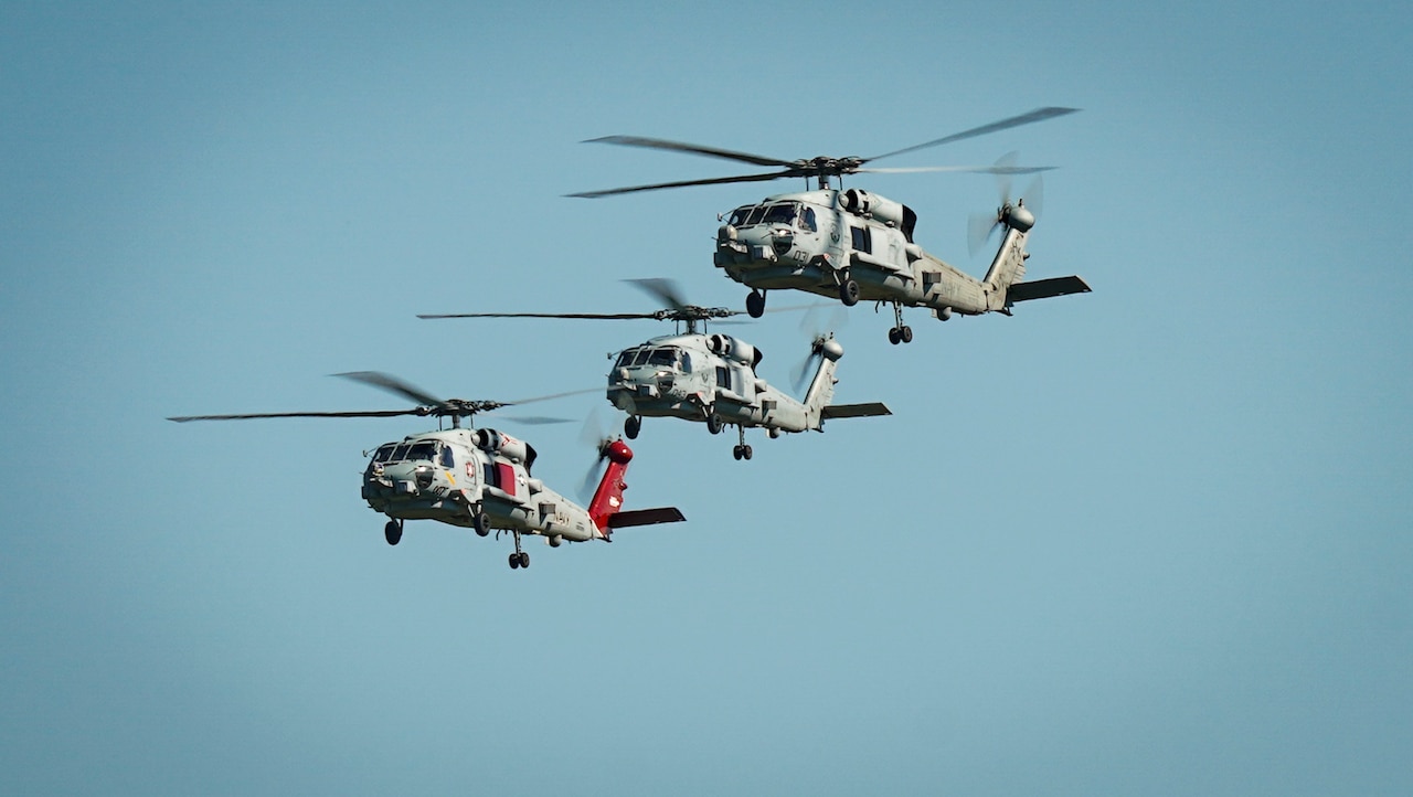 Three helicopters move in the air next to each other.