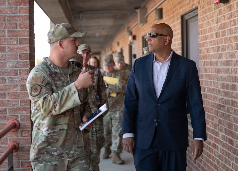 An airman walks and talks with a civilian outside a brick building.