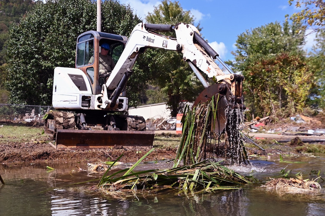 An excavator pulls weeds from a flooded area.