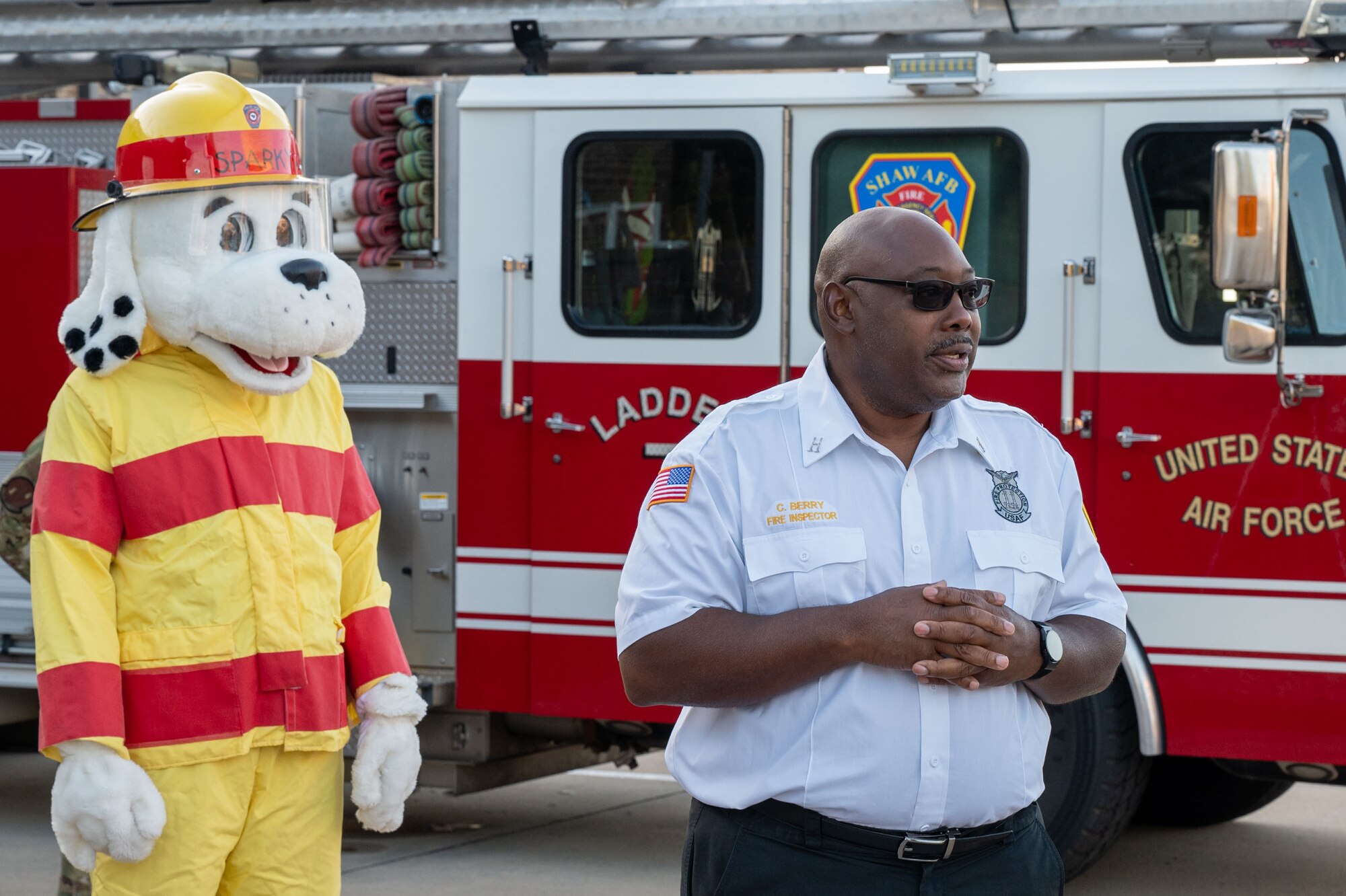 A man speaks in front of a fire truck and Sparky the Fire Dog.