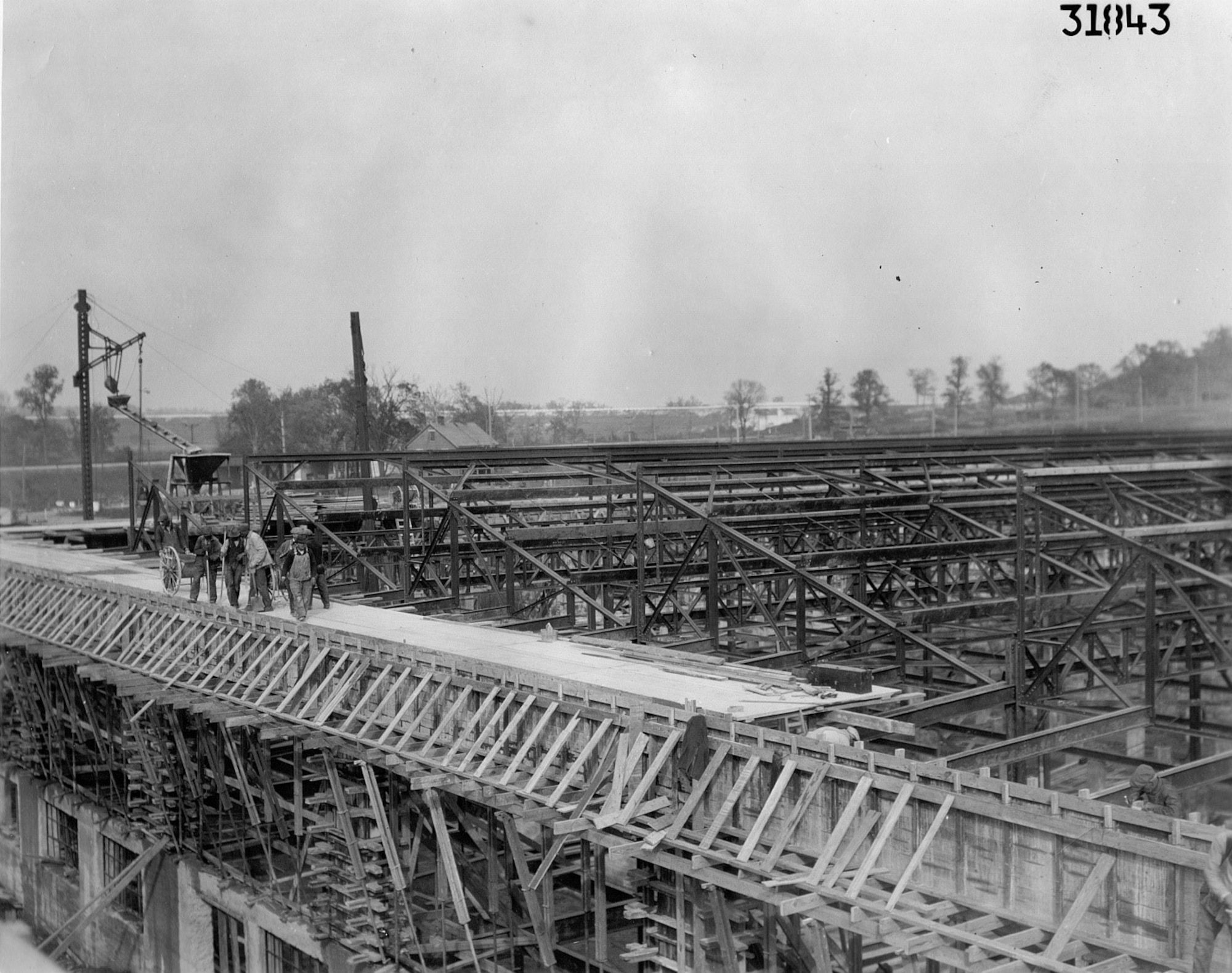 Construction workers on top of a building with wooden and steel beams surrounding them below and in the background.