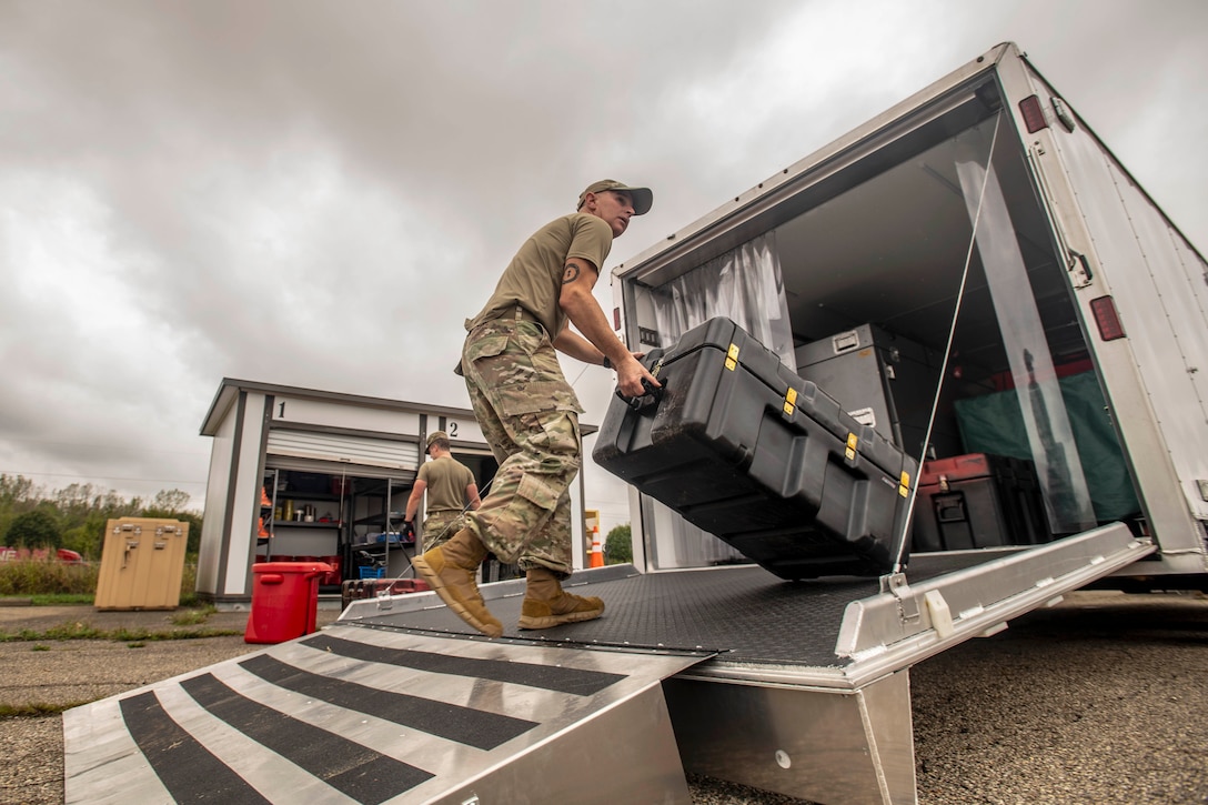 An airman carries cargo into the rear open doorway of a moving truck.