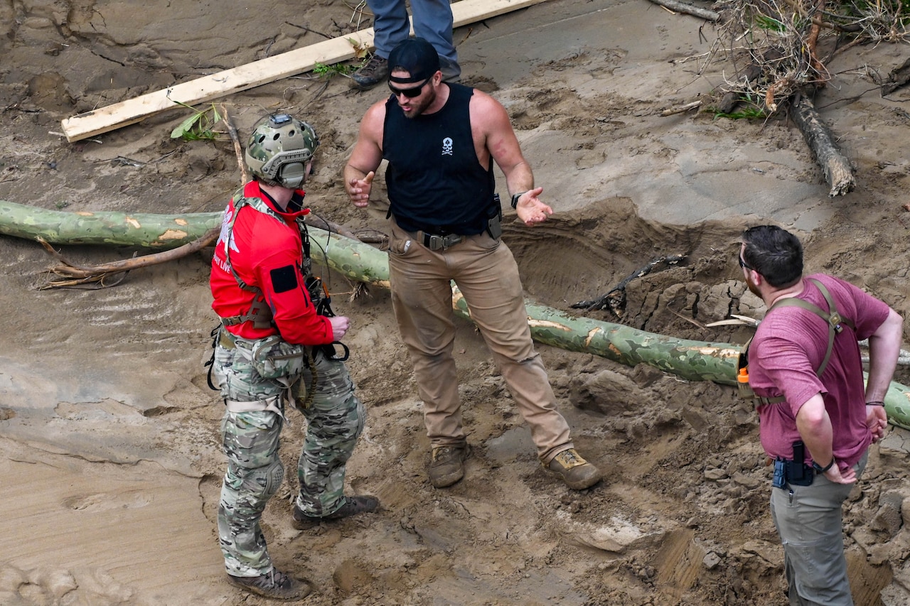 Airmen speak to civilians while standing in the mud as seen from above.