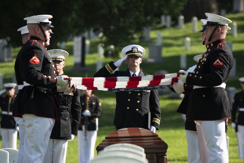 A man salutes as others fold the U.S. flag over top a casket.