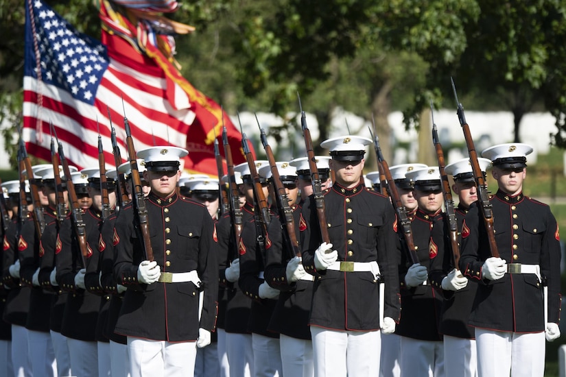 A group of Marines stand in formation with their rifles propped on their shoulders.