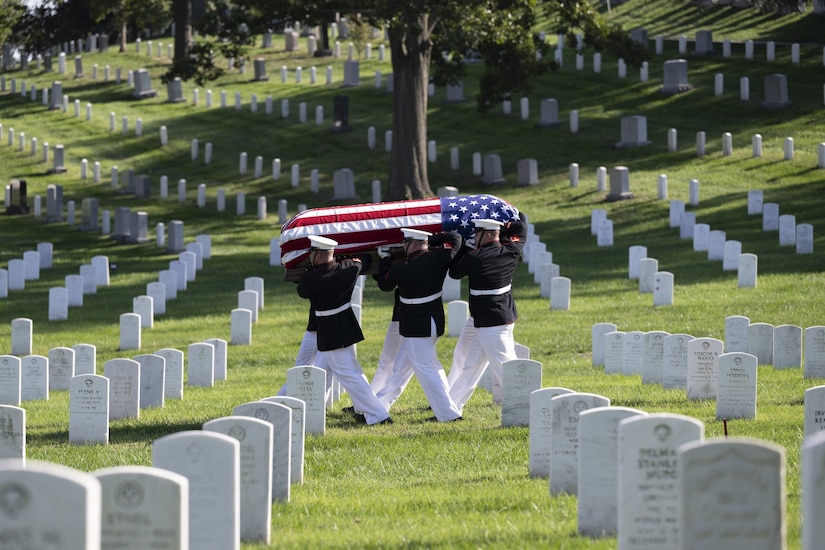 A group of Marines carry a casket through a cemetery.