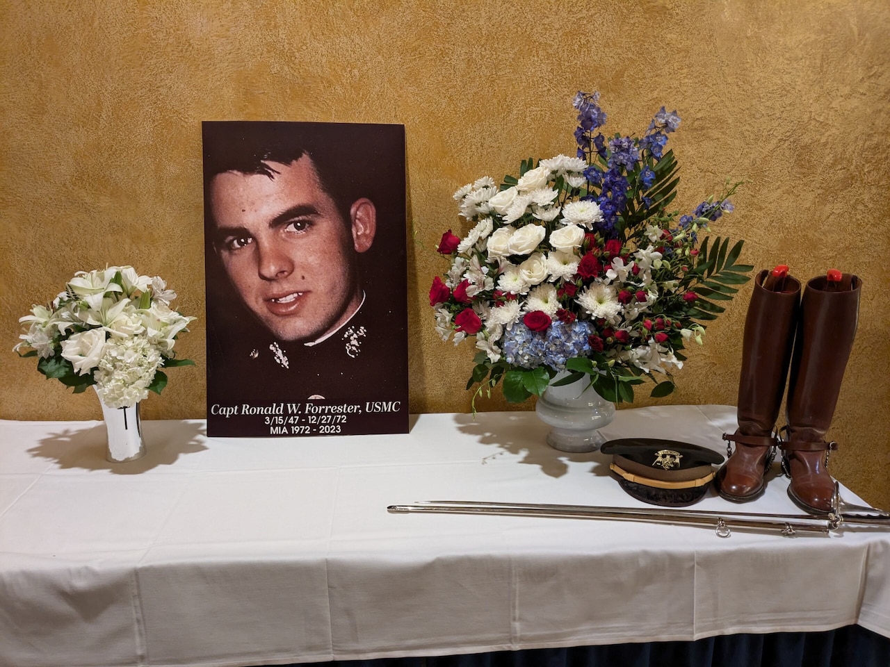 A table holds flowers, a pair of boots, and sword and a photo of a fallen Marine.