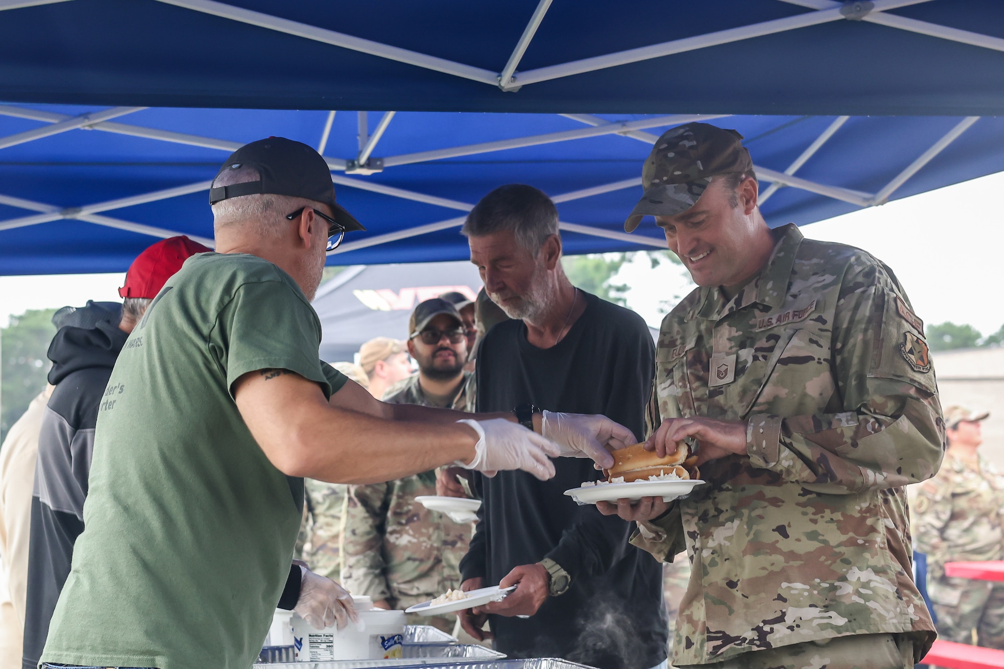 From right, U.S. Air Force Master Sgt. Keith Elliss Jr., 177th Maintenance Group Aerospace Ground Equipment mechanic, and Mr. Jack Peterson, Logistics Readiness Squadron hazmat pharmacy technician, get served food by Mr. Burt Salisbury, Veterans of Foreign Wars Post 12173 Chaplain - Army, during Community Assessment and Resilience Engagement (CARE) day at the 177th Fighter Wing, Egg Harbor Township, New Jersey, Sept. 27, 2024. CARE day is a program in which members of the 177th FW can come together to celebrate community and new partnerships. (U.S. Air National Guard photo by Airman 1st Class Connor Taggart)