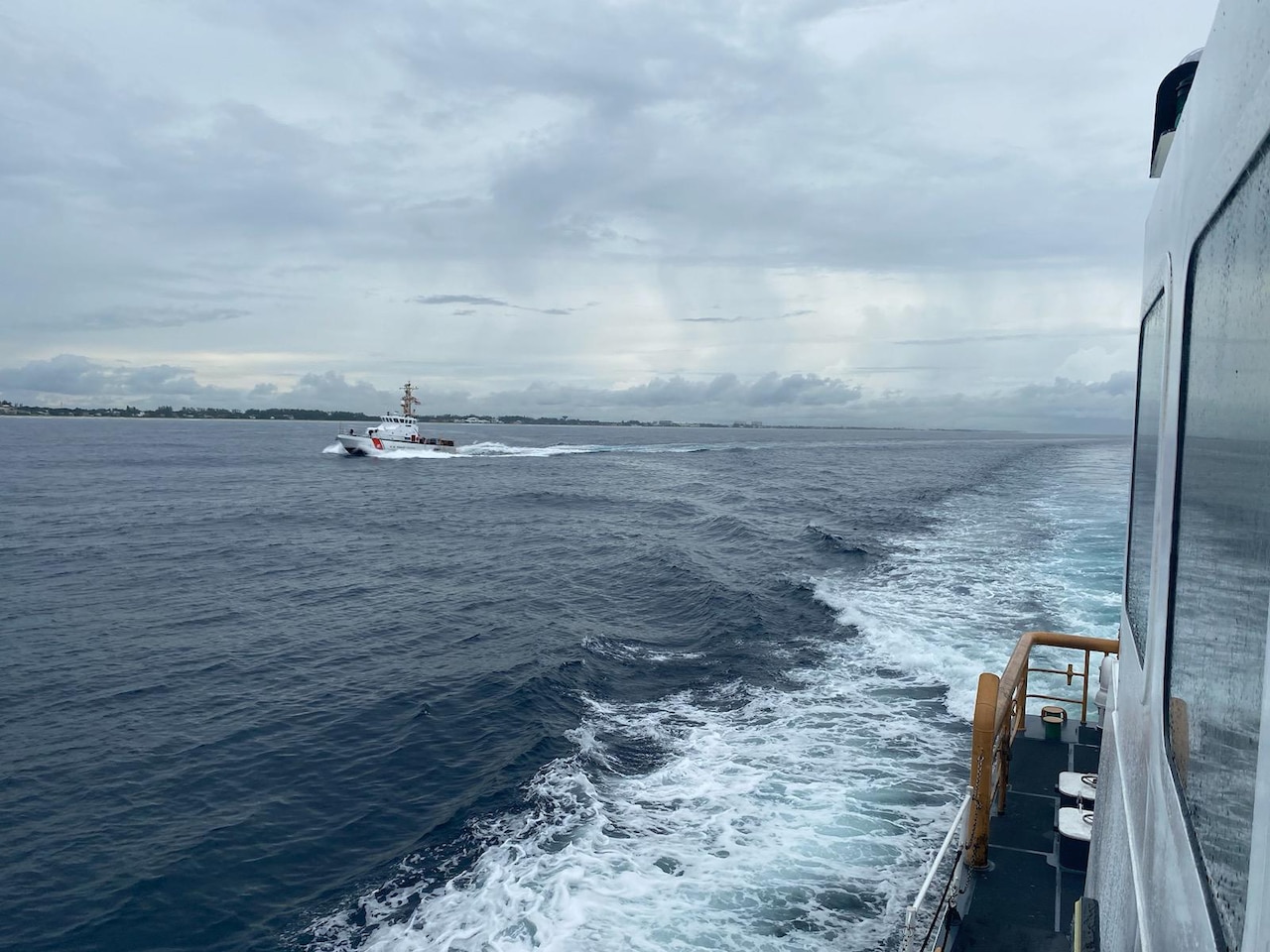 Coast Guard cutters transit water under cloudy skies.
