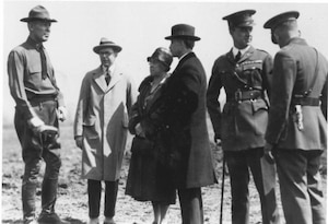 Military men and woman standing around in an empty field.