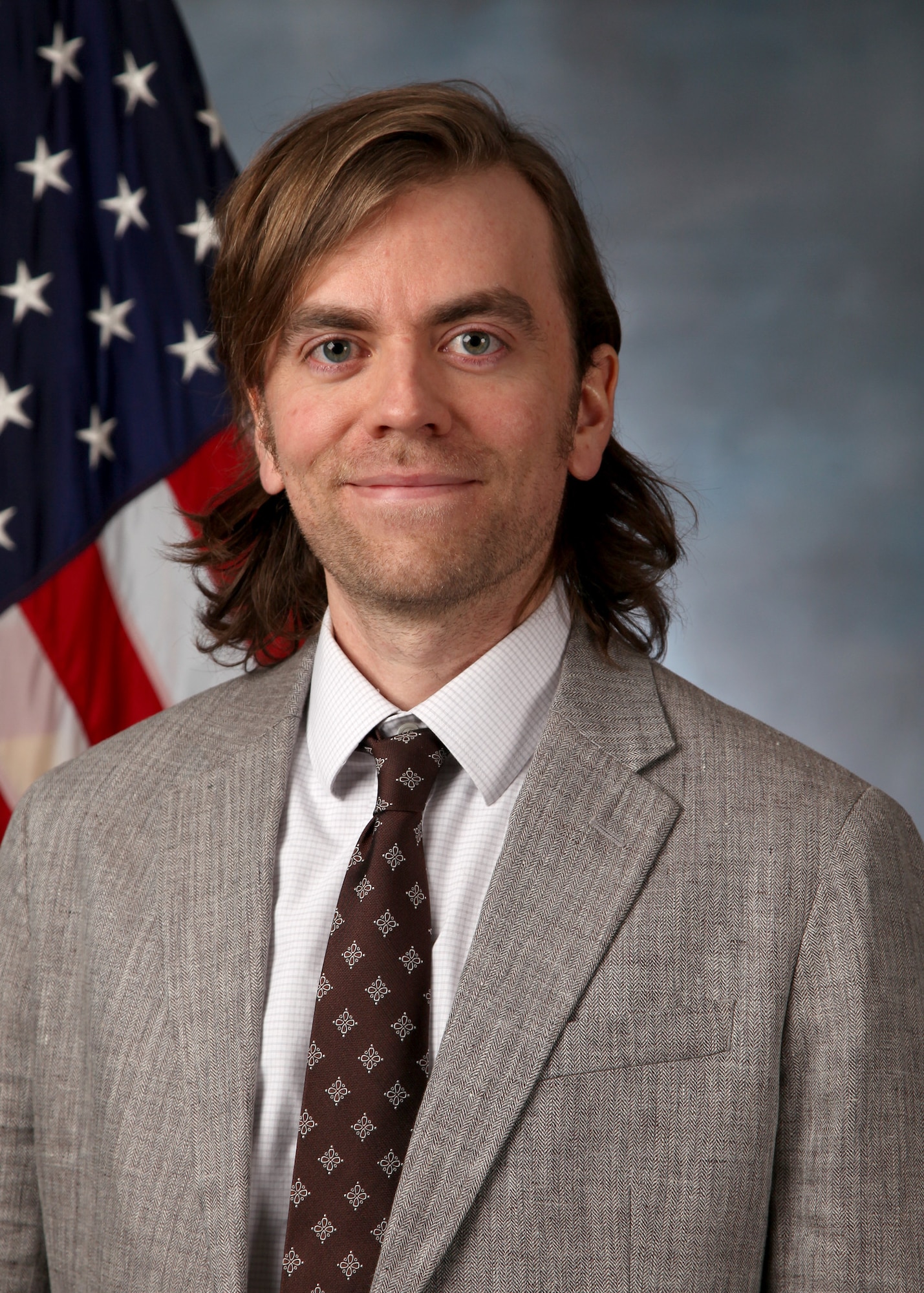 Man in business dress poses for headshot in front of flag
