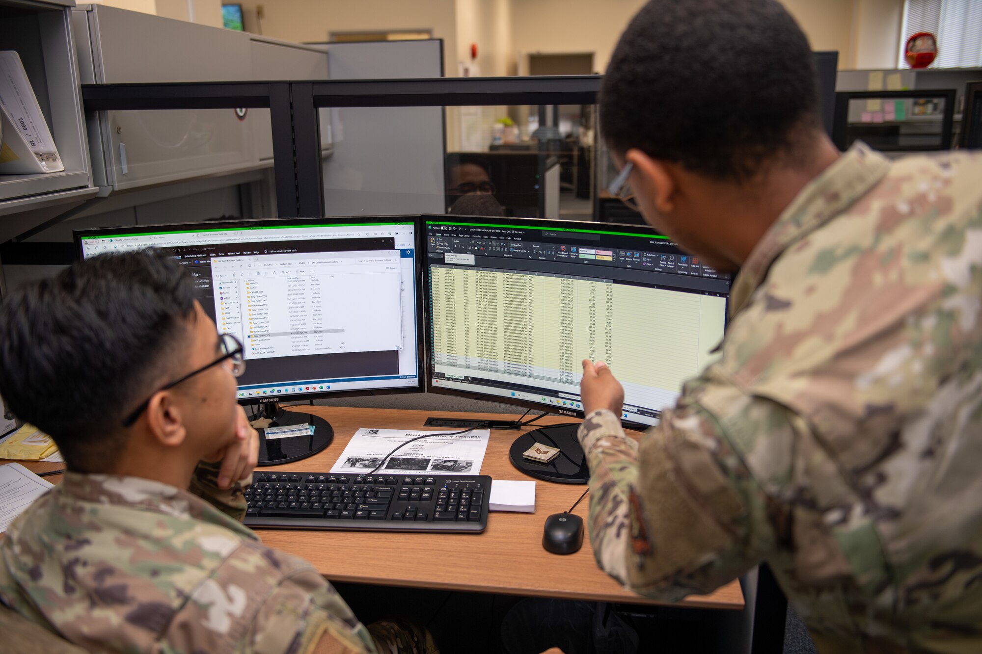 Two airmen look and discuss over finances on a computer screen in the finance office.