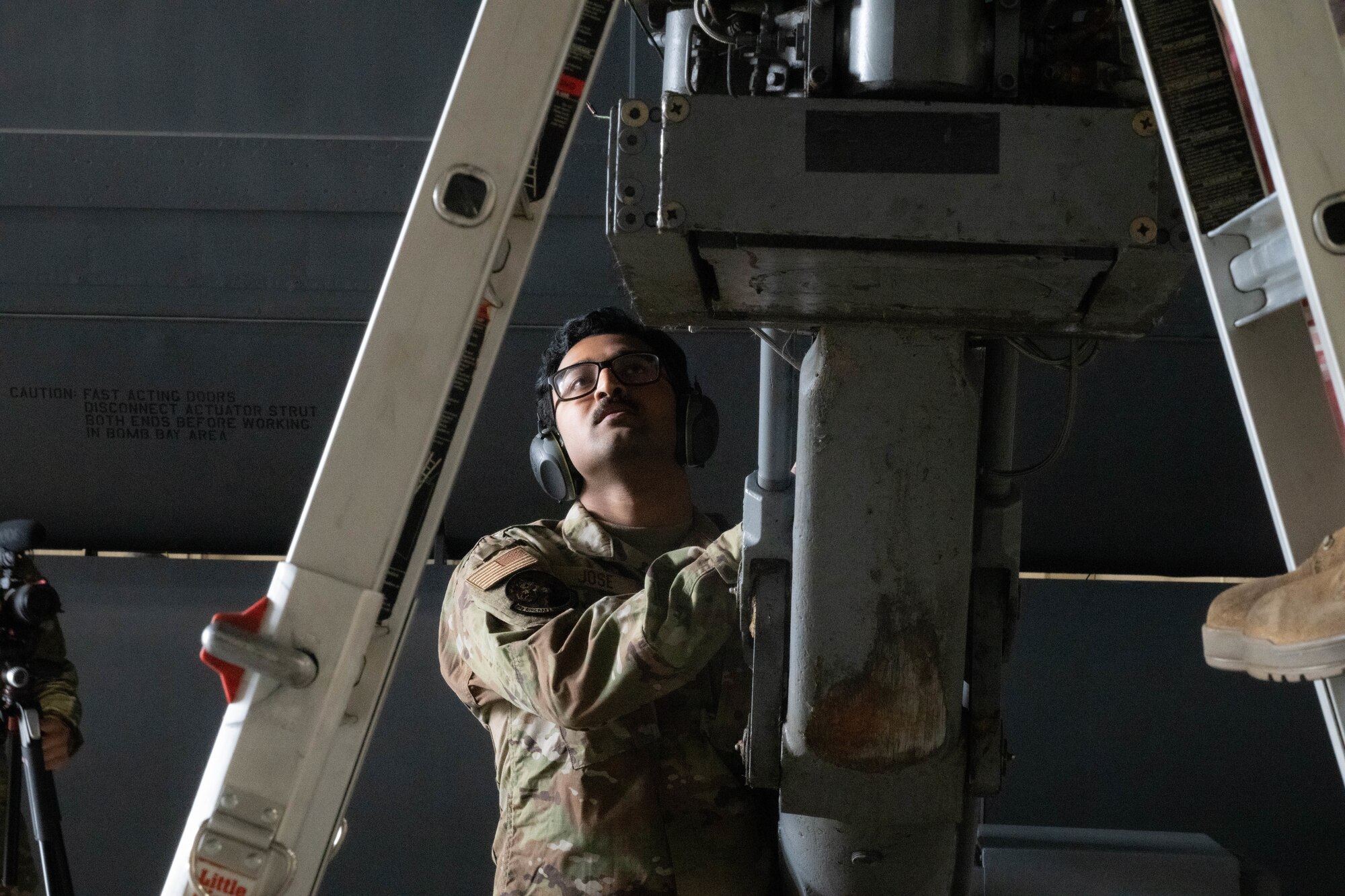 Senior Airman Christo Jose, 23rd Bomber Generation Squadron load team member, observes for safety while his teammates attach an inert GBU-31 to the underside of a B-52H Stratofortress wing at Minot Air Force Base, Oct. 4, 2024. In order to safely load the inert GBU-31 onto the aircraft, two Airmen are needed to attach it to the aircraft while another supervises to ensure safety. (U.S. Air Force photo by Airman 1st Class Wesley Davies)