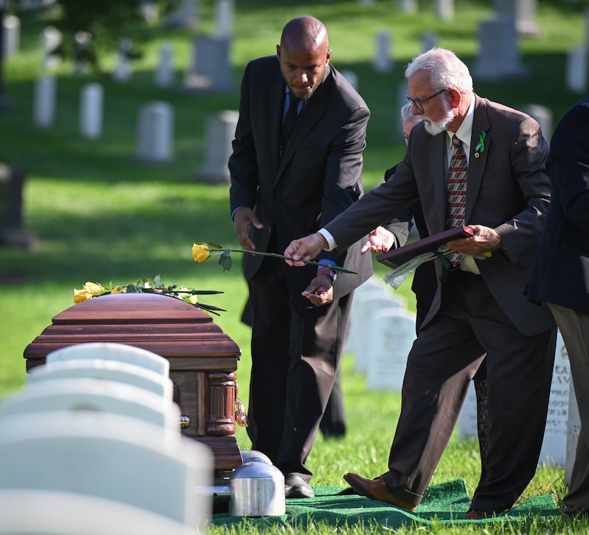 A man places a yellow rose on the top of a casket.