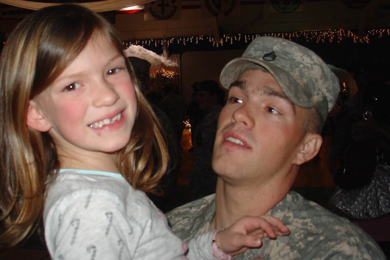 A man holds a young child who’s smiling at the camera.